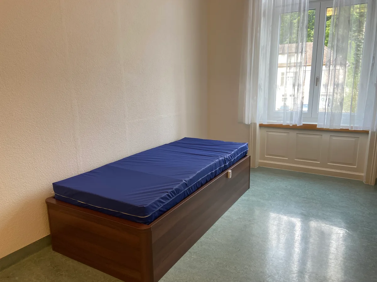 Etwas karg und doch mit Tageslicht. Das Bett in der «leichten» Isolationszelle. Ein Bett mit blauer Matratze steht in einem leeren Raum.